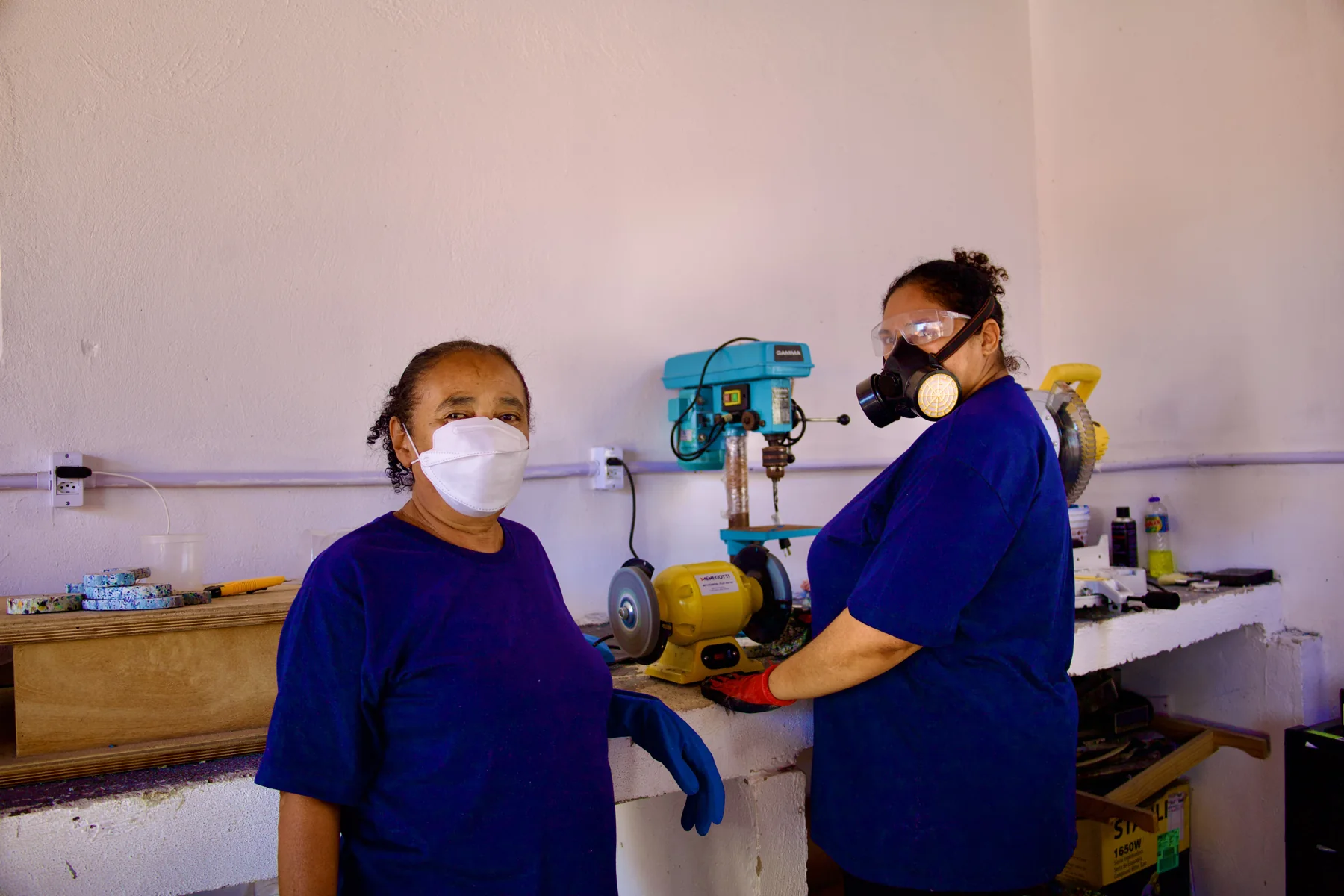 Duas artesãs trabalhando juntas com equipamentos de proteção na oficina